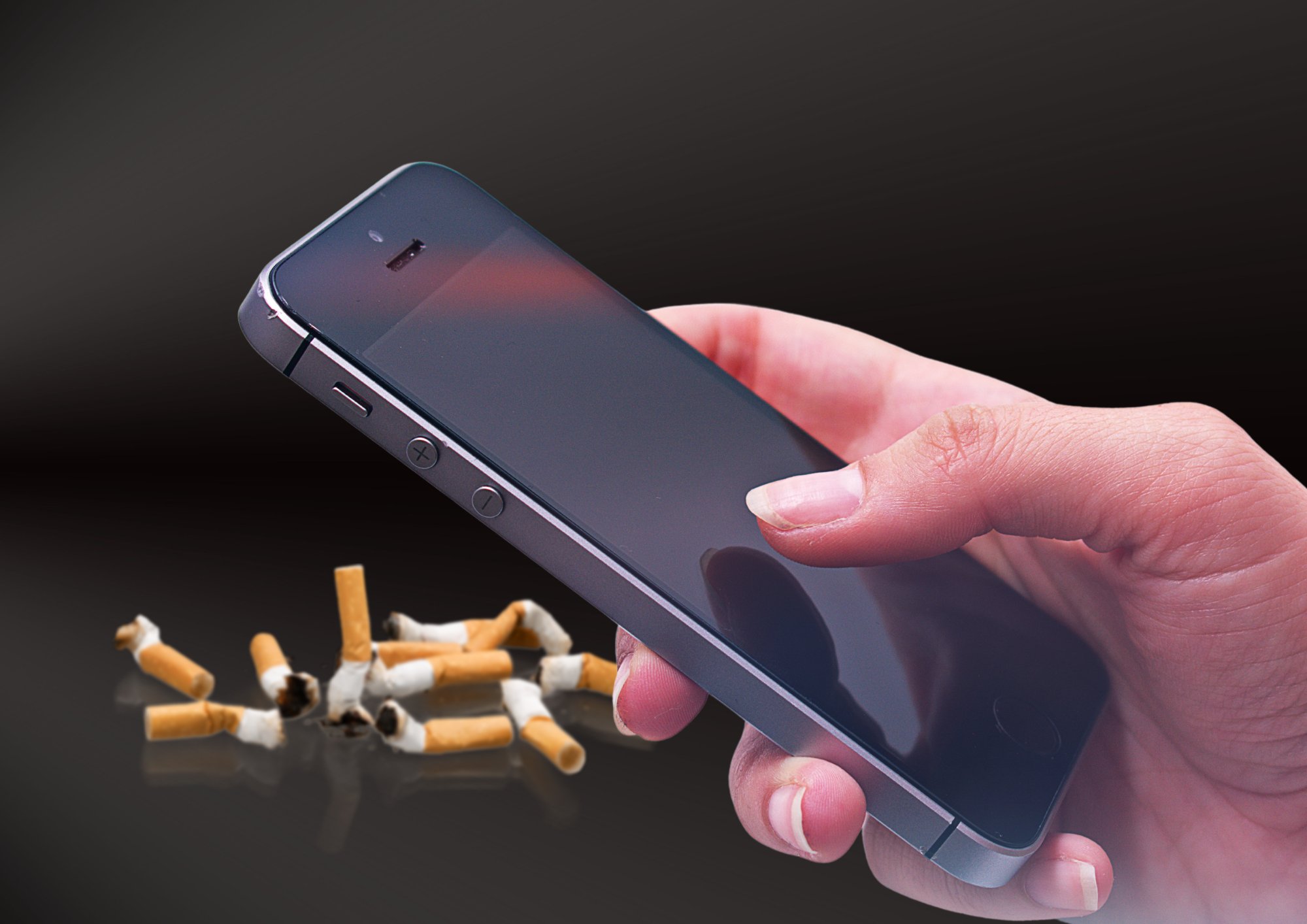 A hand holding a mobile phone with crushed cigarettes in the background