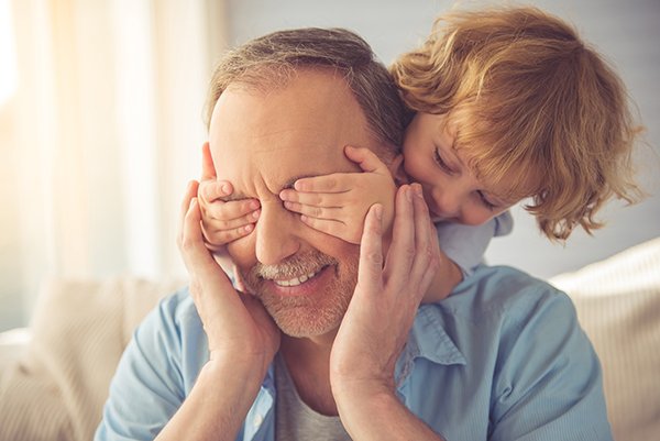 Photo of young child blindfolding grandfather with her hands. Photo credit is Getty Images.