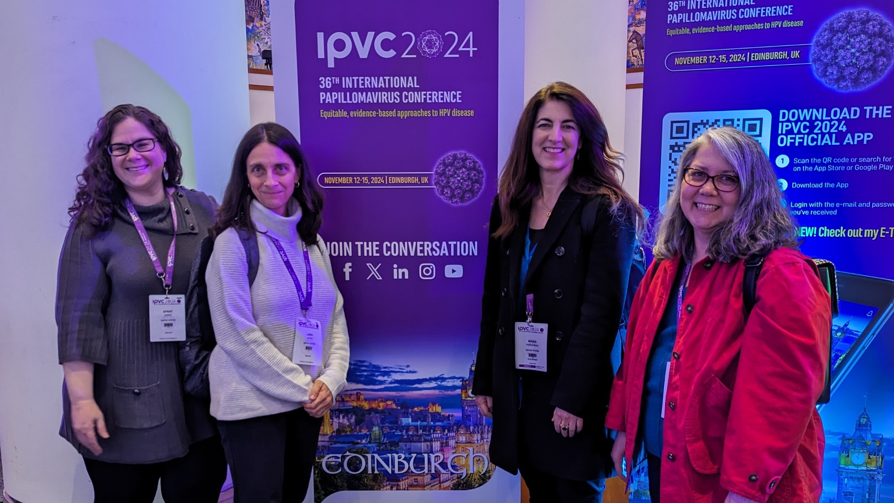 Two women stand on either side of a banner promoting a conference.