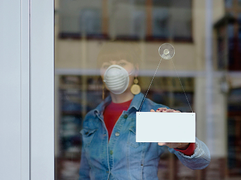 A woman wearing a mask prepares to open up her business. Photo by Getty Images.