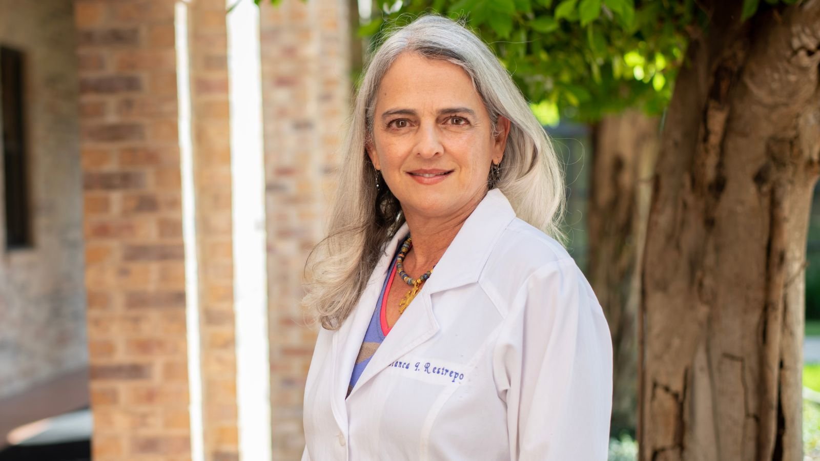 Blanca Restrepo pictured in white coat in front of tree in foreground.