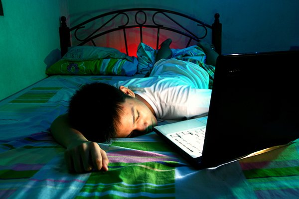 Photo of boy lying on bed asleep in front of a laptop computer. Photo credit is Getty Images.