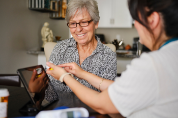 Nurse shows medication to an older woman in her house