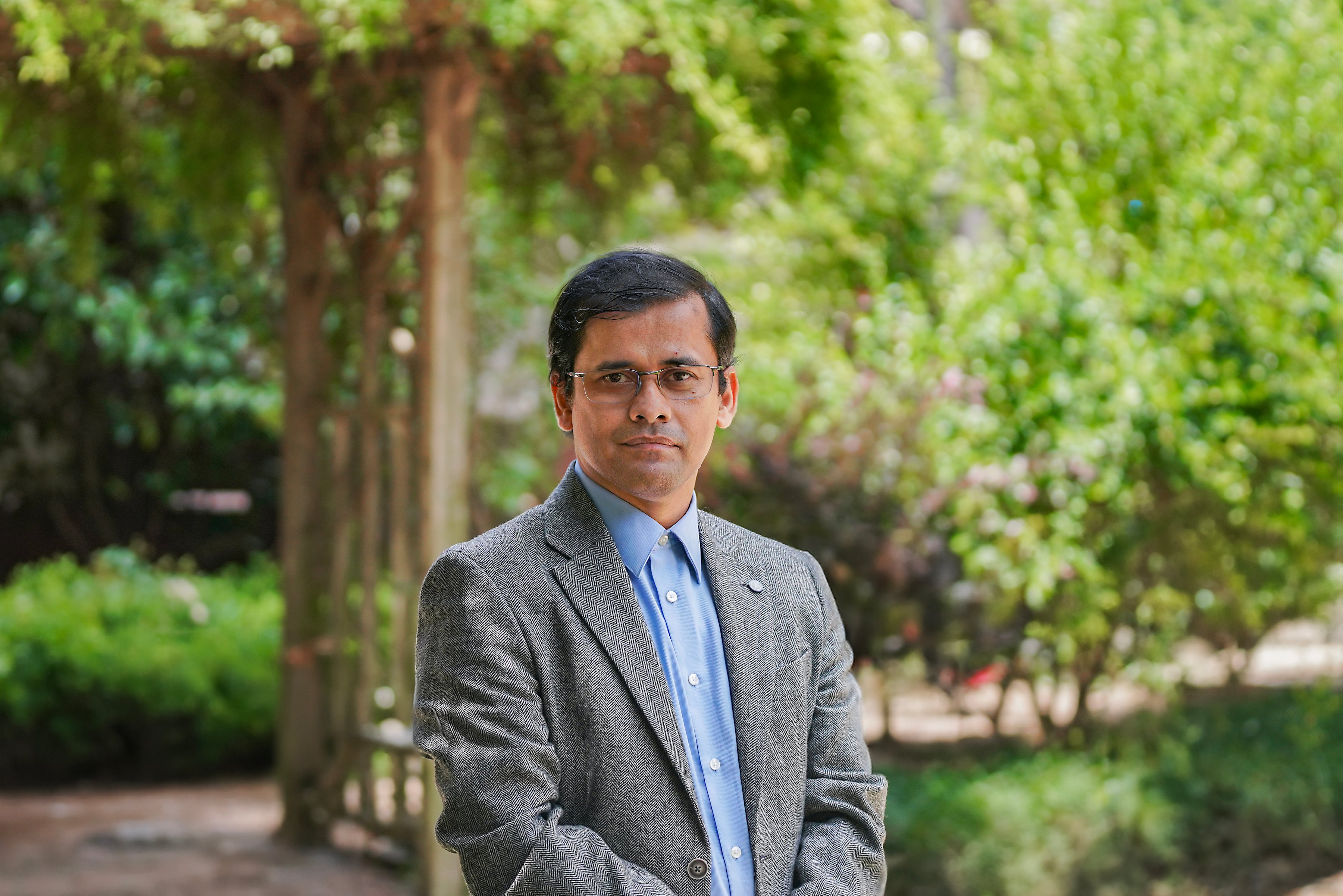 Samiran Ghosh in front of Holistic Garden with hanging trees and greenery.