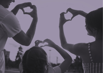 A man, a woman, and a young girl use their hands to make heart shapes against the sky