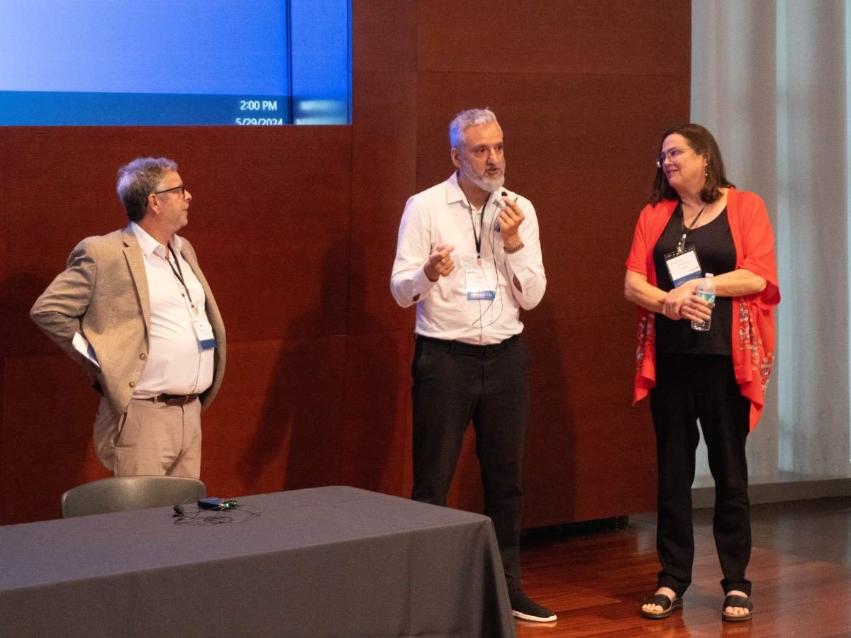 Doctors Adolfo Rubinstein, Rodrigo Reis, and Valerie Paz-Soldan standing and speaking at the front of the auditorium.