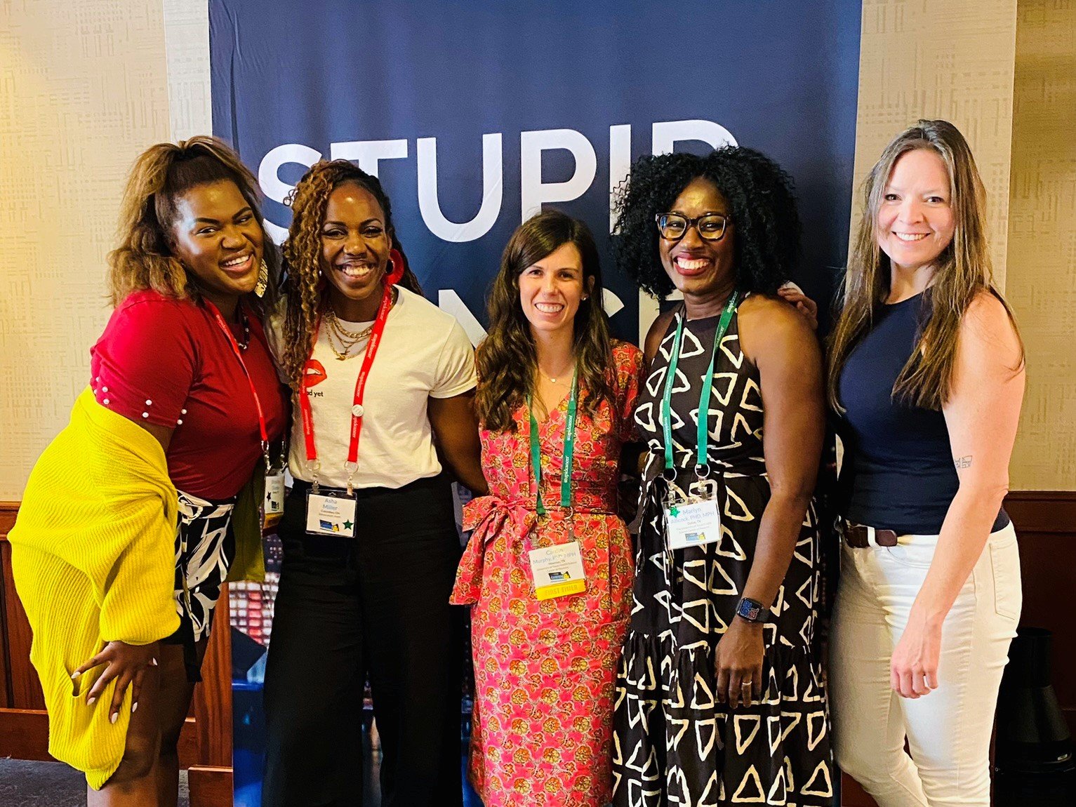 Five women posing together at a meeting.