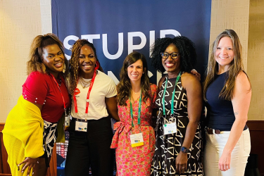 Five women posing together at a meeting.