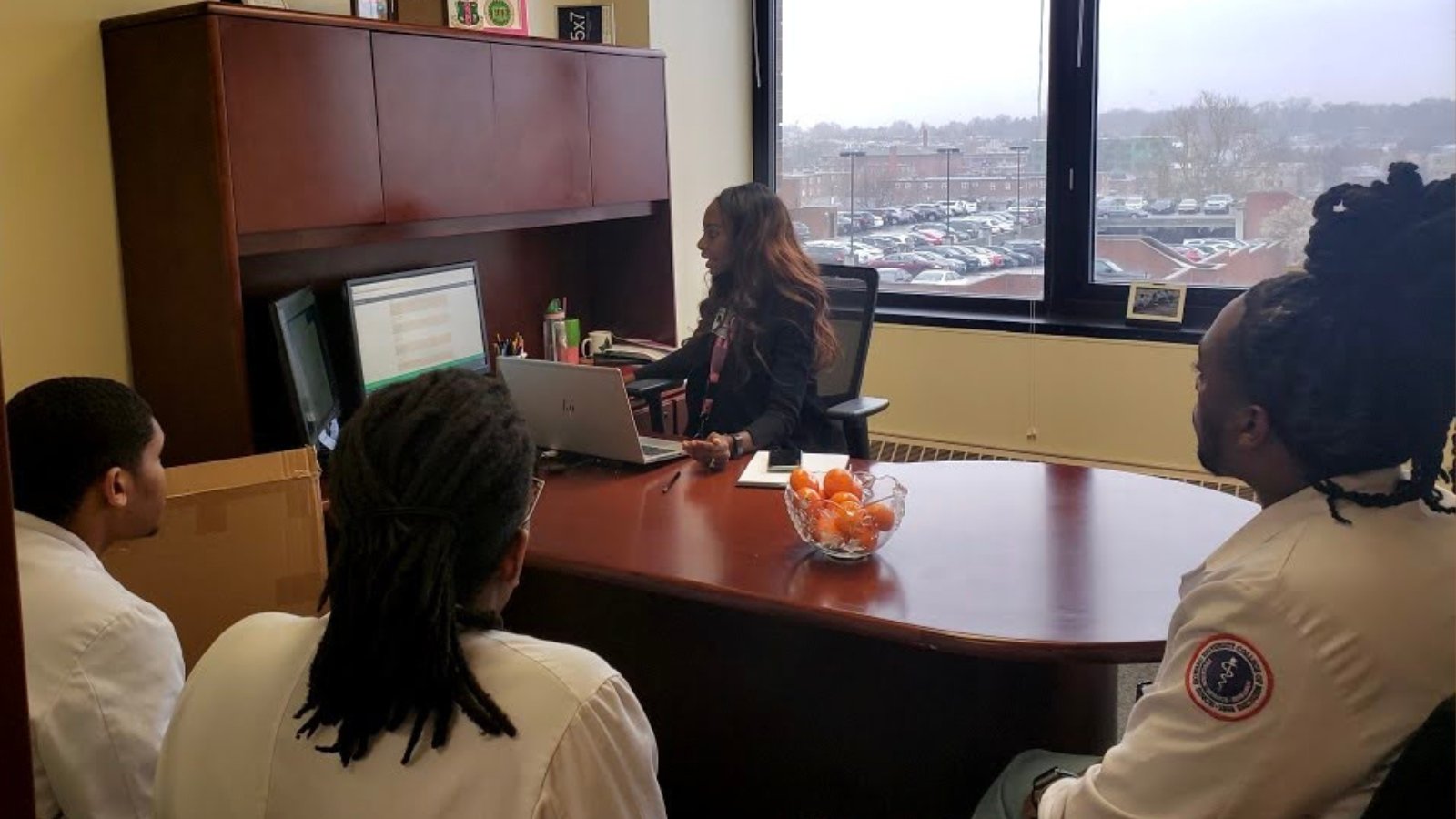 Amanda Valentine pictured in front of desk with three students in lab coats.