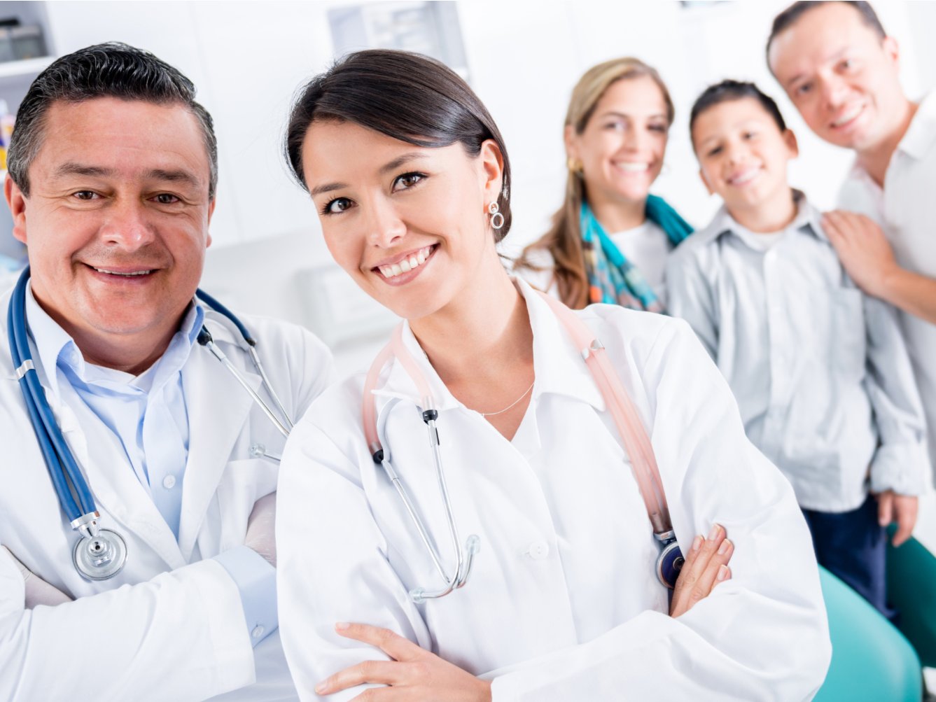 A family of two parents and a child in a doctor's office with two doctors, all smiling at camera.