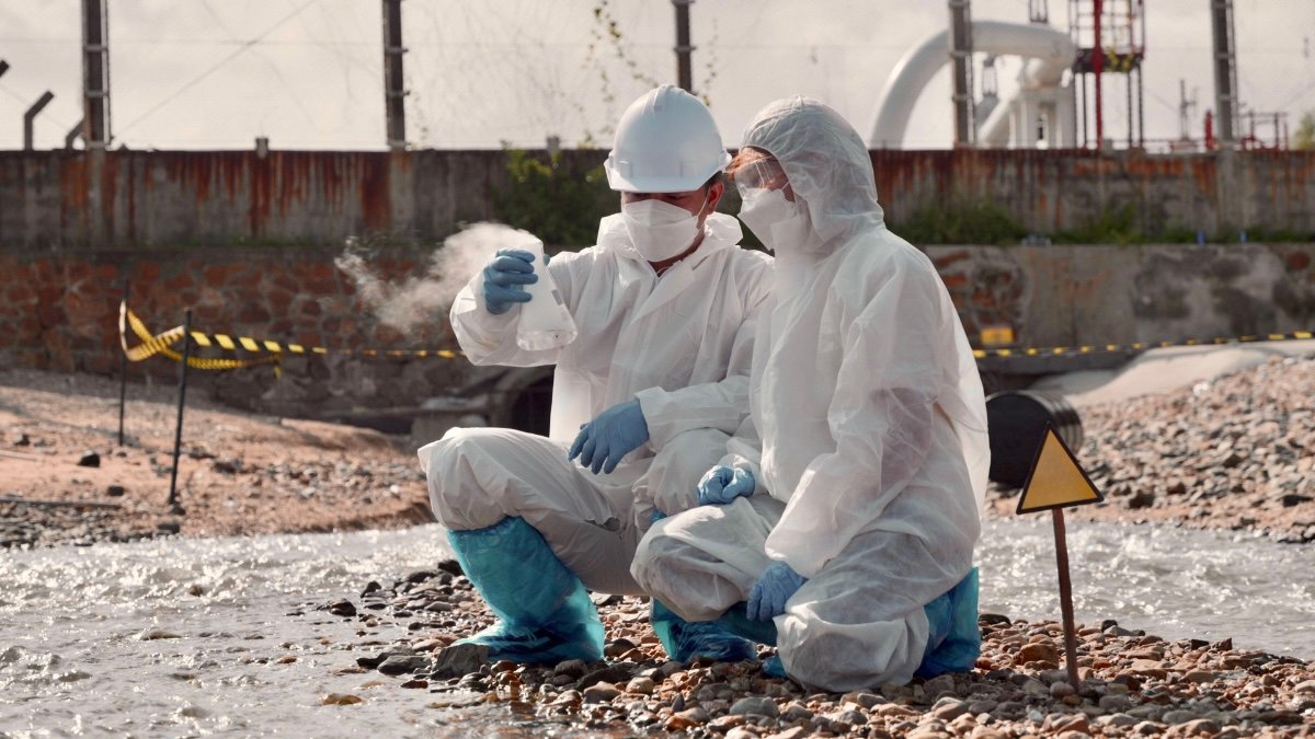 Two people in protection gear sampling wastewater.