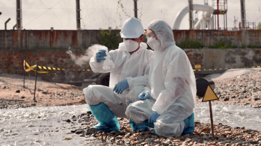 Two people in protection gear sampling wastewater.