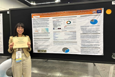 Paola Hernandez holding award certificate in front of research poster.