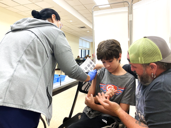 A father talks to his son as the boy prepares to receive a vaccination from a health care professional.