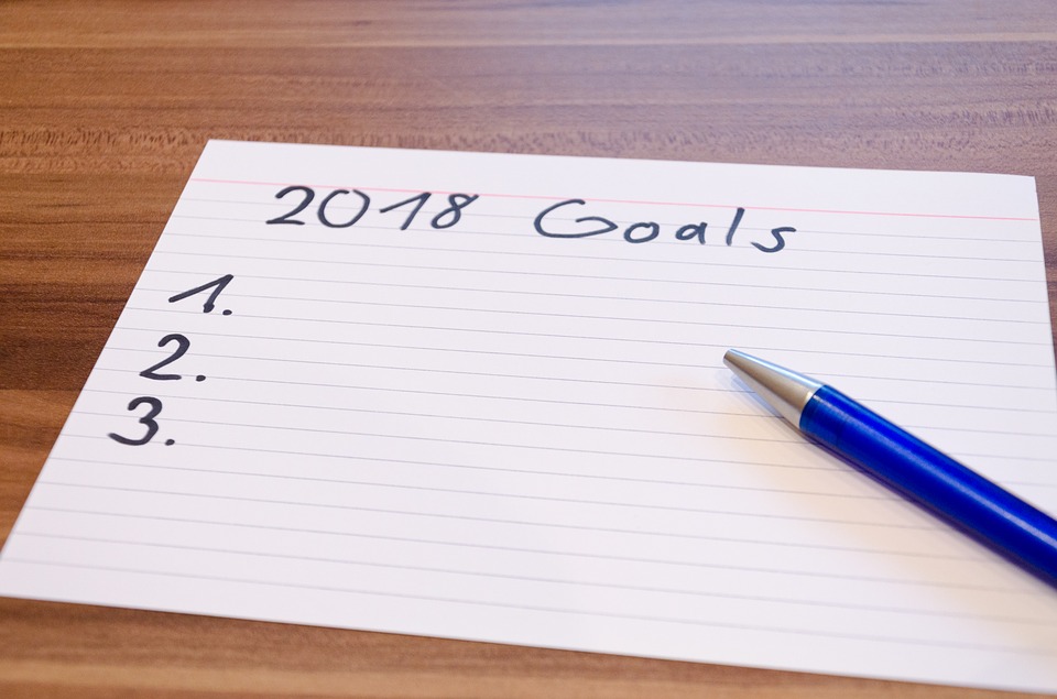 notecard and a pen. notecard reads 2018 Goals with a numbered list