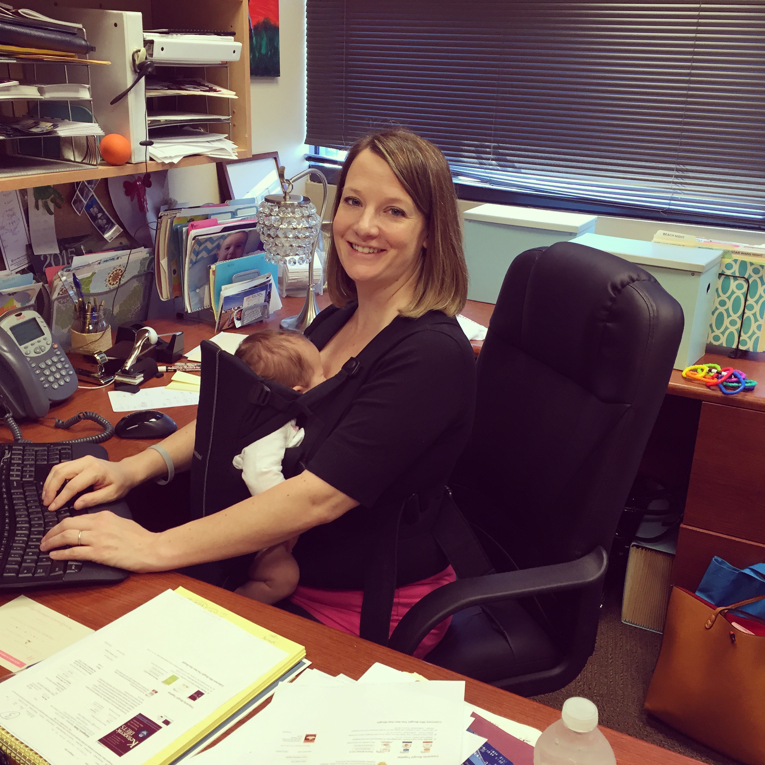 woman working at desk with a baby strapped to chest