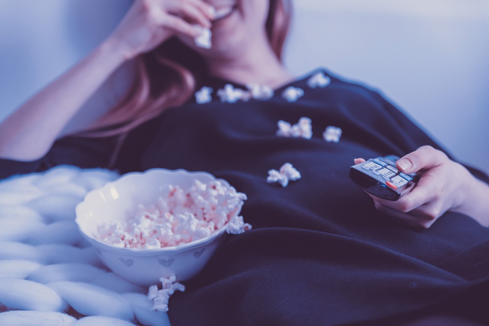 woman laughing eating popcorn while laying down with a remote