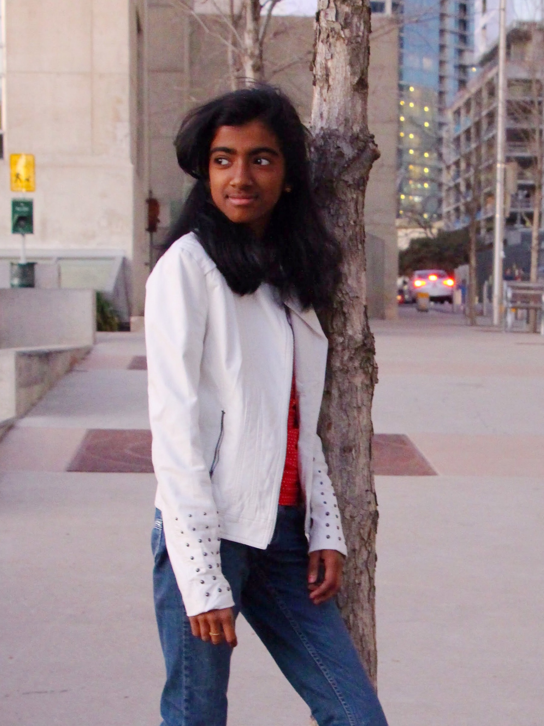 girl in white jacket leaning against tree